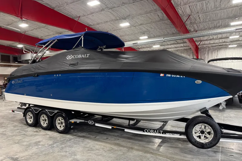 Slide: The Image of 2011 Cobalt boat with blue hull and black cover on a trailer indoors. - 18