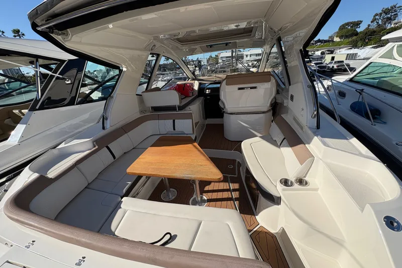 Slide: The Image of 2018 Sea Ray Sundancer 350 Coupe interior with seating and wooden table in marina setting. - 7