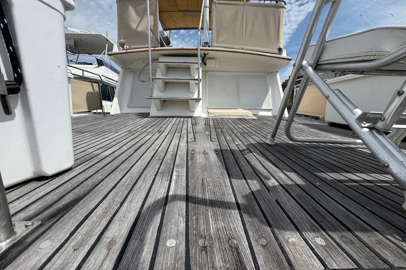 Slide: The Image of 1989 Grand Banks 42 Motor Yacht deck with wooden flooring and stairs under a blue sky. - 27