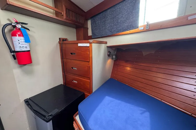 Slide: The Image of 1989 Grand Banks 42 Motor Yacht cabin with wooden drawers, bed, and fire extinguisher. - 58