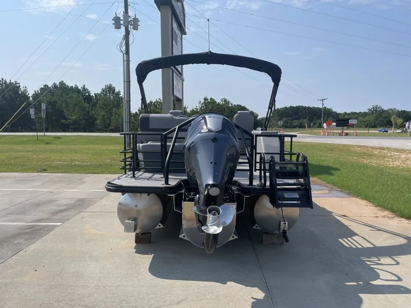 Slide: The Image of A 2026 Starcraft EXS 3 Q DH pontoon boat is parked on a lot. It features an outboard motor and a black canopy. - 2