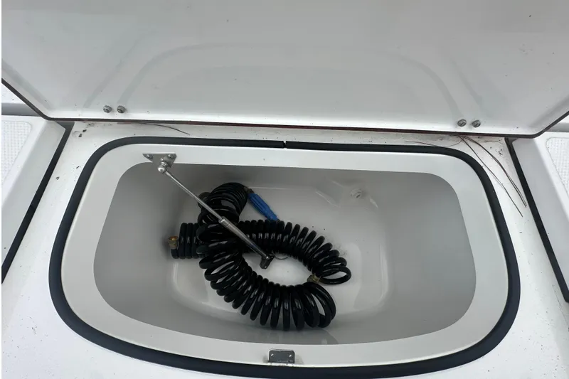 Slide: The Image of Open storage compartment on 2022 BlackJack 256 Bay boat with coiled hose inside. - 9