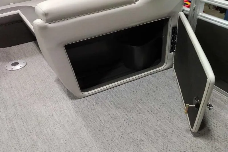 Slide: The Image of 2026 Sun Tracker Fishin' Barge 22 XP3 storage compartment with open door on carpeted floor. - 120