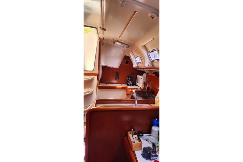 Slide: The Image of Interior of 1999 Beneteau Oceanis 321 sailboat, featuring a compact kitchen and wooden cabinetry. - 19