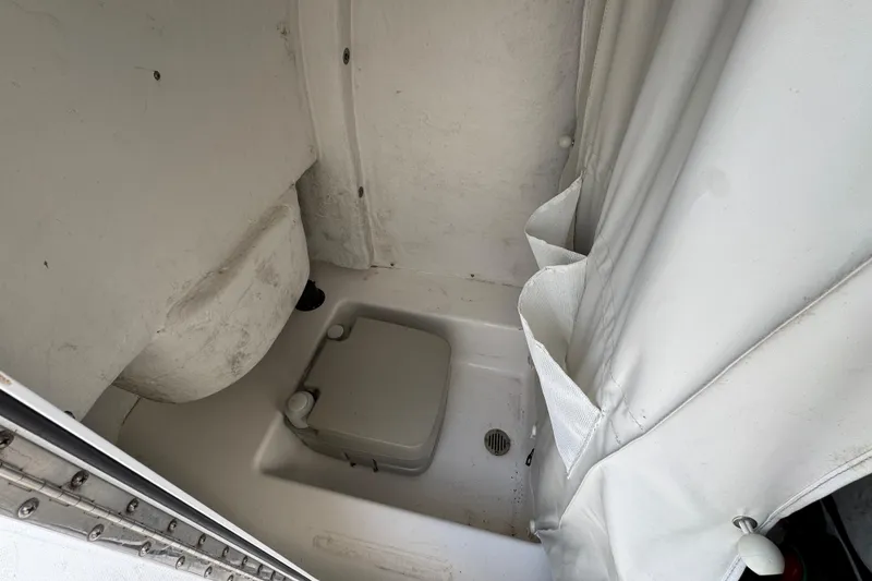Slide: The Image of 2017 Tidewater 230 CC Adventure boat interior with compact toilet and white curtain. - 18