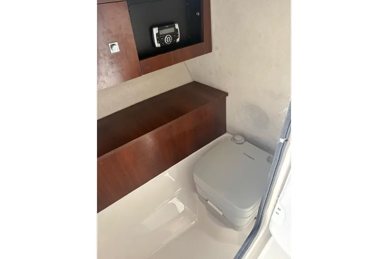 Slide: The Image of 2020 Robalo R227 Dual Console interior with portable toilet and wooden cabinetry. - 7