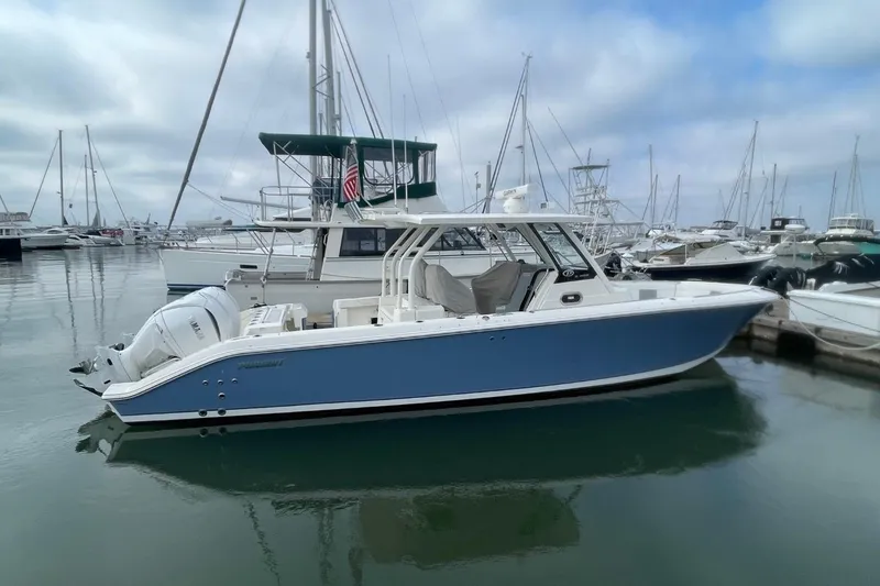 Slide: The Image of 2021 Pursuit S 328 Sport boat docked in a marina, surrounded by other vessels. - 2