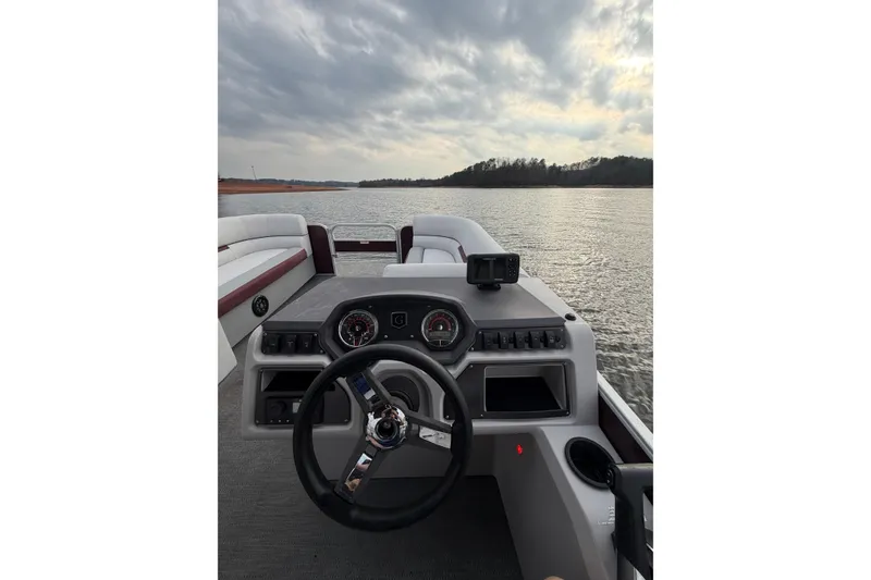 Slide: The Image of 2023 Godfrey Sweetwater 2286 C boat interior with steering wheel and dashboard on a lake. - 9