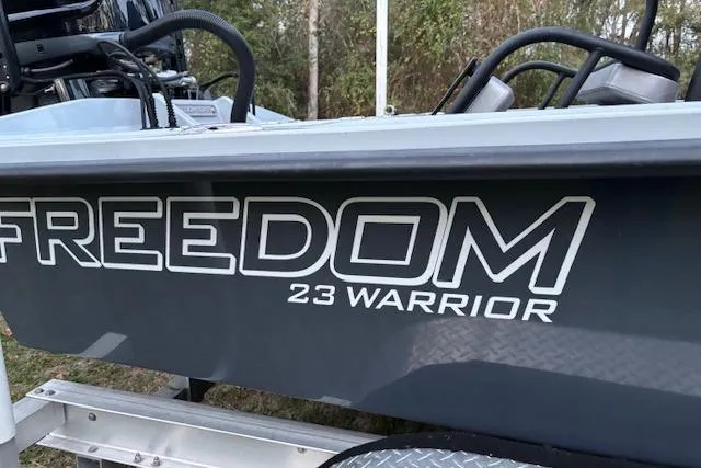 Slide: The Image of 2025 Freedom Boats 23' Warrior, side view with logo, parked outdoors. - 8