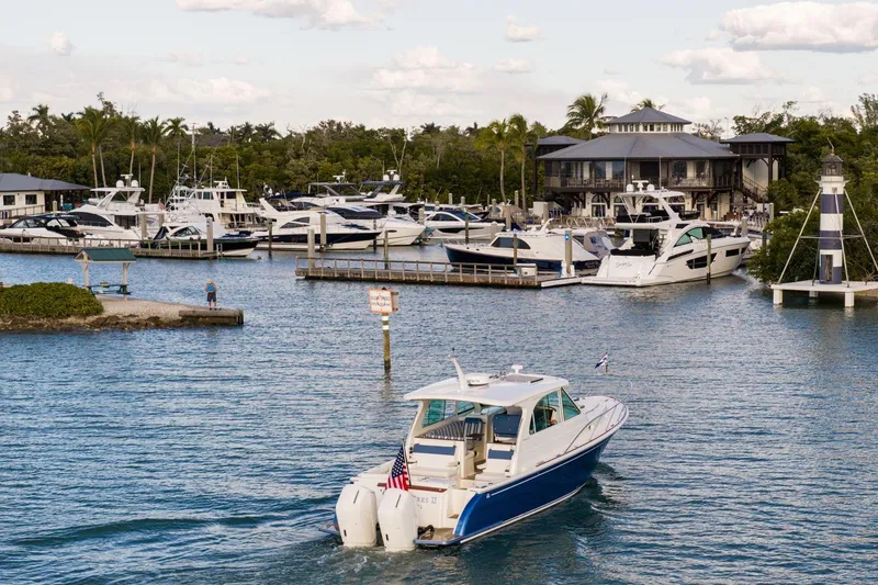 Slide: The Image of 2025 Hinckley Sport Boat 40 X cruising near marina with lighthouse and docked boats. - 13
