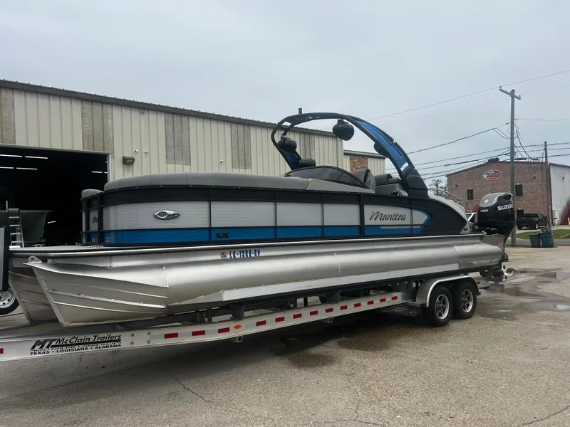 The Image of 2022 Manitou 27 pontoon boat on trailer outside industrial building. - 1