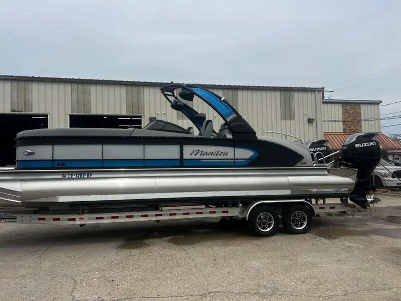 Slide: The Image of 2022 Manitou 27 pontoon boat on trailer, parked outside a warehouse. - 14