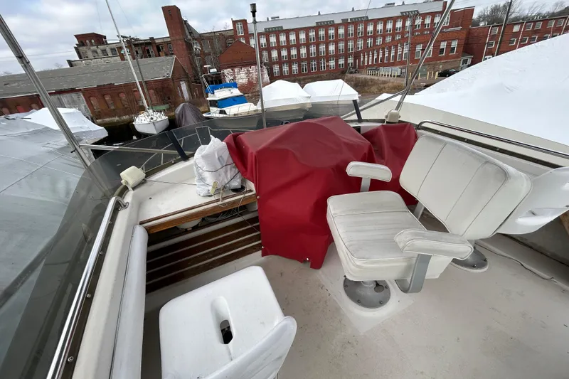 Slide: The Image of 1983 Silverton 34 Convertible boat interior with white seating and red cover, docked near brick buildings. - 13