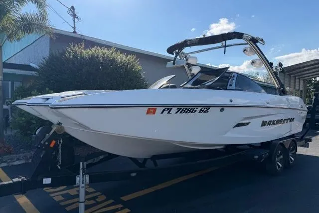 Slide: The Image of 2013 Malibu Wakesetter 24 MXZ boat on trailer, parked outdoors under clear sky. - 2