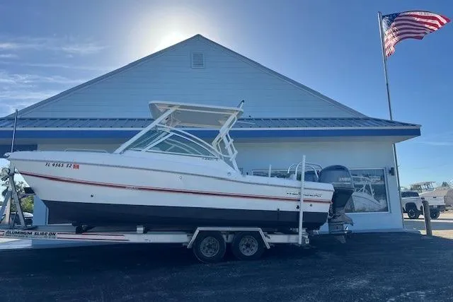 The Image of 2021 World Cat 230 DC boat on trailer, parked outside building with American flag. - 1