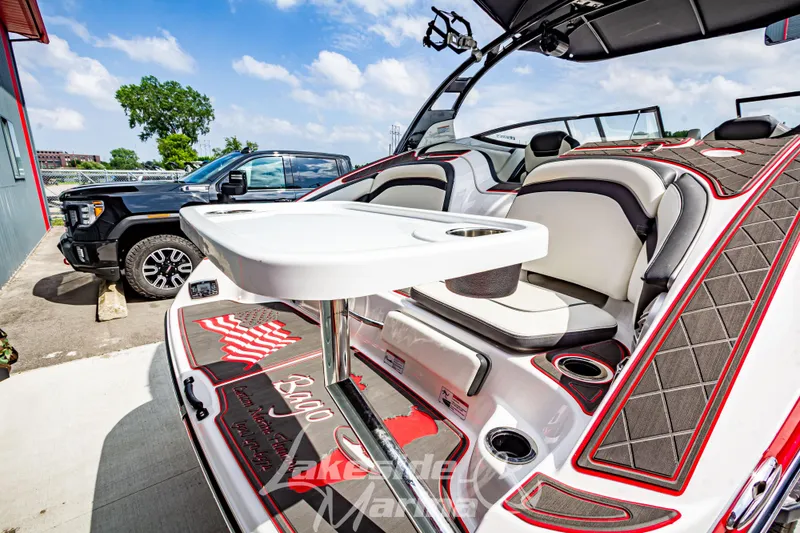 Slide: The Image of 2016 Yamaha Boats 242 Limited S E-Series interior with seating and table, parked beside a truck. - 10