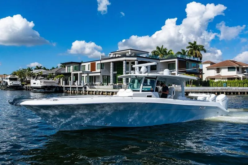 Slide: The Image of 2024 HCB 42 Lujo boat cruising near luxury waterfront homes under blue sky. - 2