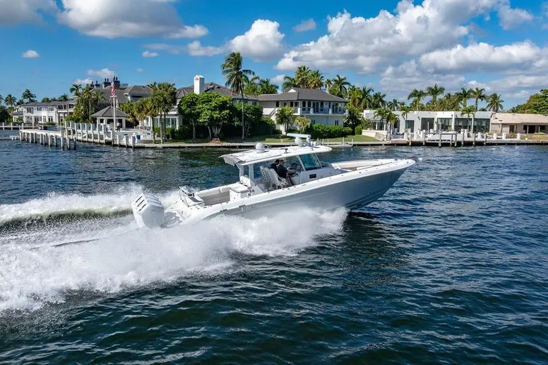 Slide: The Image of 2024 HCB 42 Lujo boat cruising on a sunny waterfront with palm trees. - 24