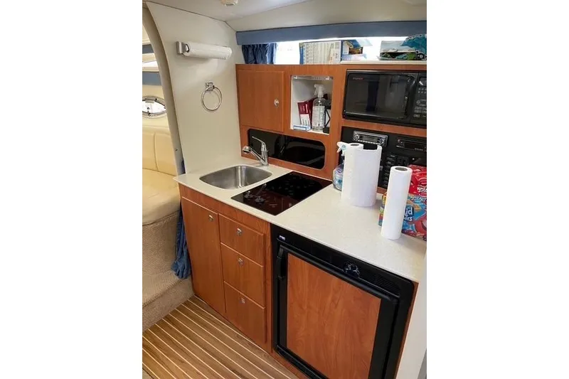Slide: The Image of 2007 Bayliner 325 boat kitchen with sink, stove, microwave, and wooden cabinetry. - 9