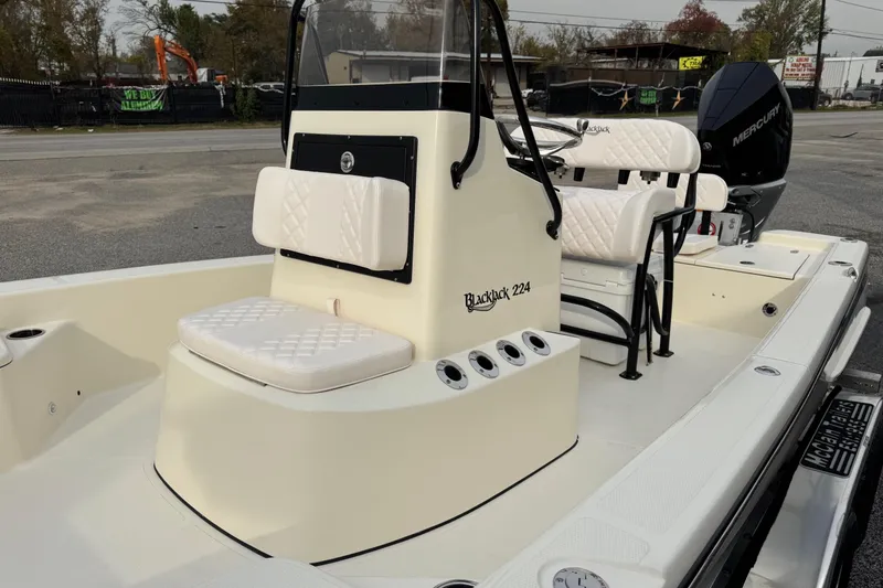 Slide: The Image of 2026 BlackJack 224 boat with white seating and Mercury engine, parked outdoors. - 12