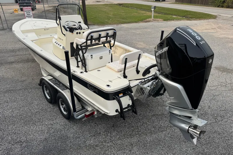 Slide: The Image of 2026 BlackJack 224 boat with Mercury engine on a trailer, parked on asphalt. - 2