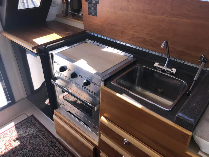 Slide: The Image of Compact kitchen in 2016 Cutwater 30 Command Bridge with stove, sink, and wooden cabinetry. - 27
