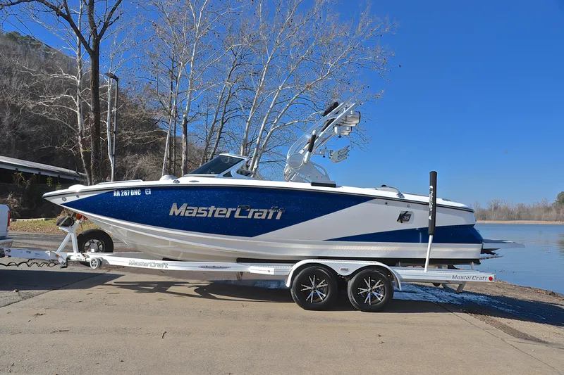 Slide: The Image of 2013 MasterCraft X-35 boat on trailer by a lake, clear blue sky background. - 12