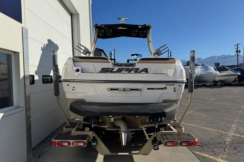 Slide: The Image of 2023 Supra SL 575 boat rear view, parked outdoors, showcasing sleek design and features. - 2