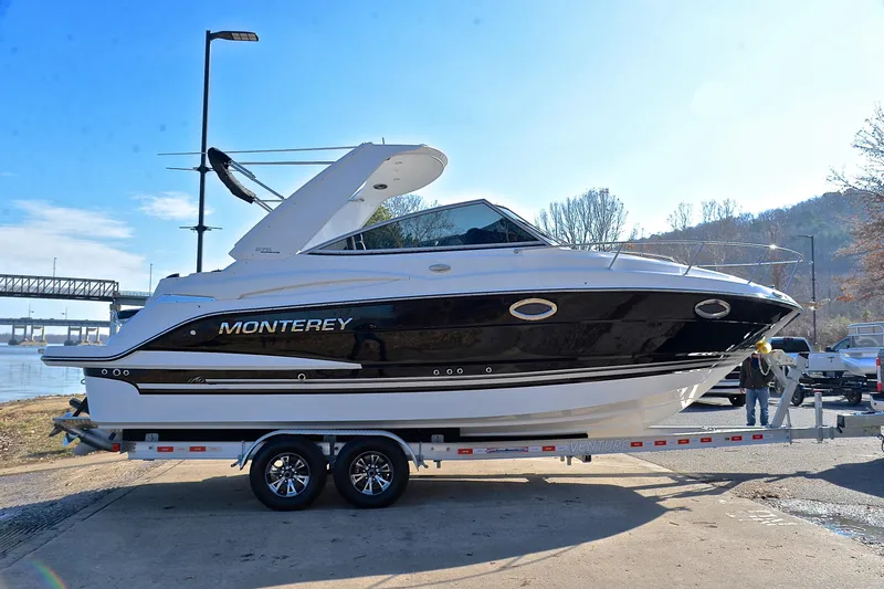 Slide: The Image of 2018 Monterey 275 Sport Yacht on trailer by riverside, under clear blue sky. - 18
