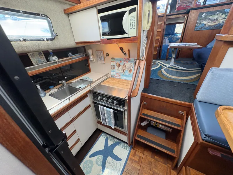 Slide: The Image of 1988 Carver 36 Aft Cabin kitchen with stove, sink, and microwave, featuring wooden cabinetry. - 39