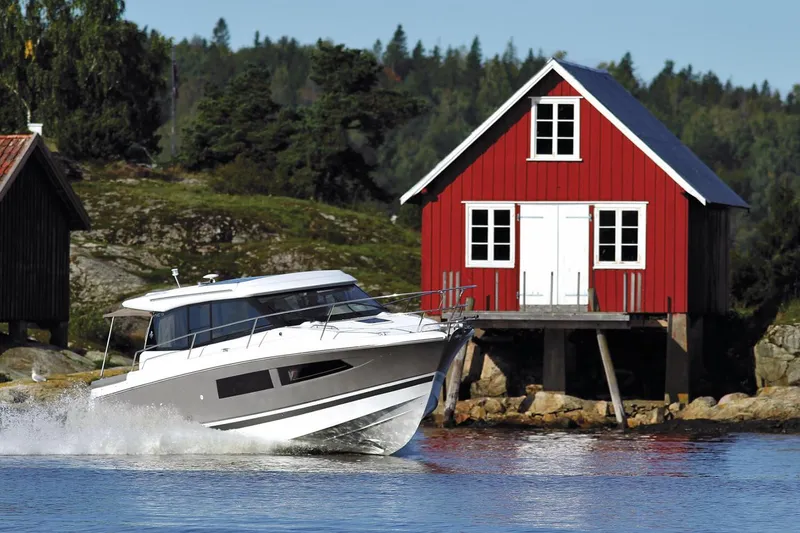 Slide: The Image of Manufacturer Provided Image: 2018 Jeanneau NC 9 boat cruising near a red lakeside cabin. - 15