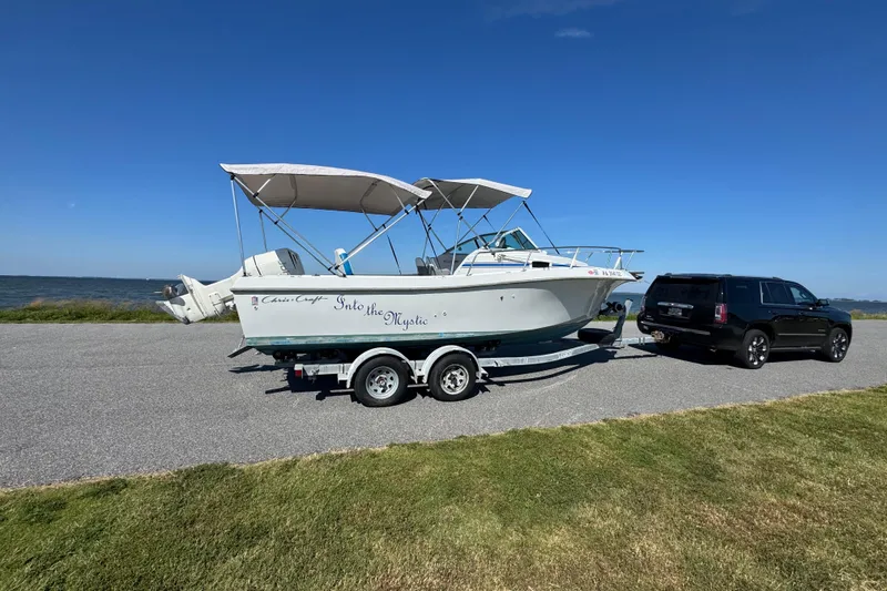 Slide: The Image of 1988 Chris-Craft 215 Sea Hawk boat on trailer, hitched to a black SUV, near a waterfront. - 14