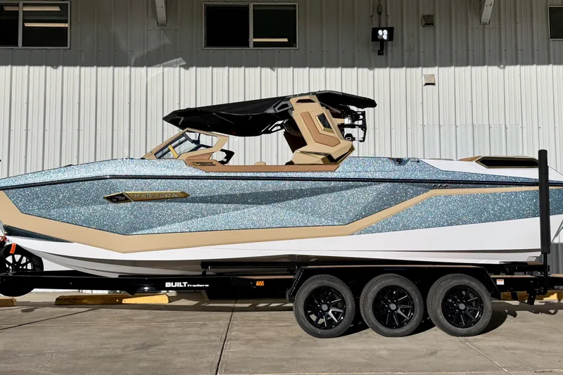 Slide: The Image of 2026 Nautique Super Air Nautique G25 Paragon boat on trailer, metallic blue and beige design. - 1