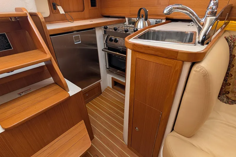 Slide: The Image of 2021 Catalina 315 yacht interior kitchen with wooden cabinetry, stainless steel appliances, and compact design. - 8