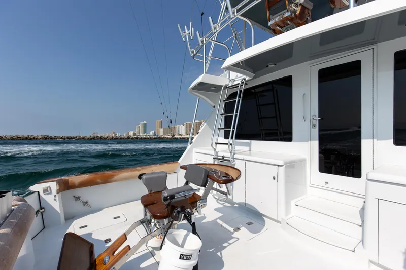 Slide: The Image of 2003 Hatteras 60 Convertible at sea, featuring fishing chair and city skyline. - 14