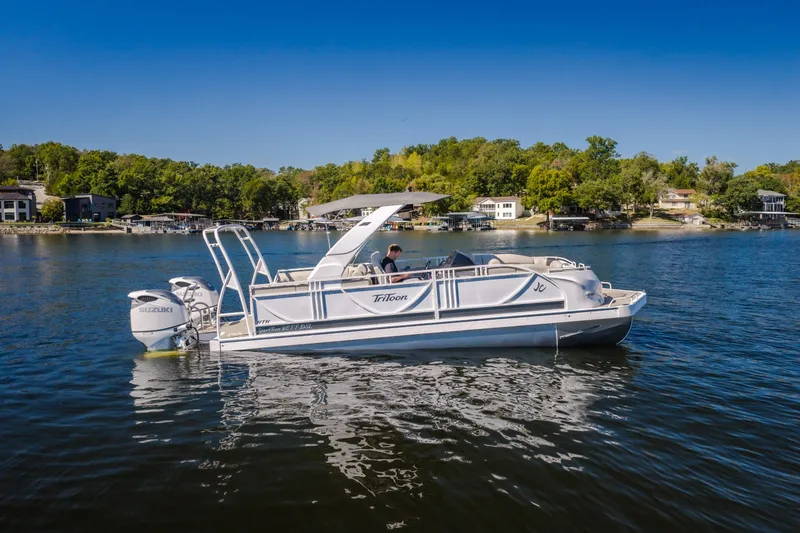 Slide: The Image of 2026 JC Sporttoon 26TT pontoon boat on a serene lake with lush shoreline. - 1