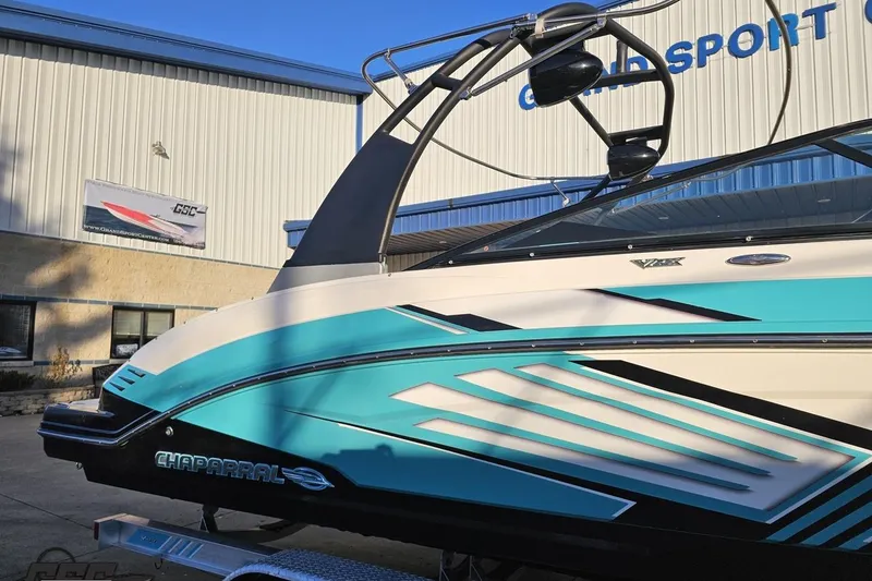 Slide: The Image of 2016 Chaparral Vortex 243 VRX boat with vibrant blue and white design, parked outside a building. - 4