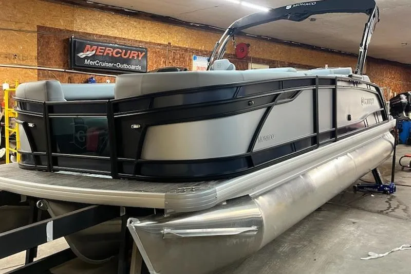 Slide: The Image of 2026 MONACO 235SFL pontoon boat in a garage, featuring sleek design and Mercury outboard signage. - 2