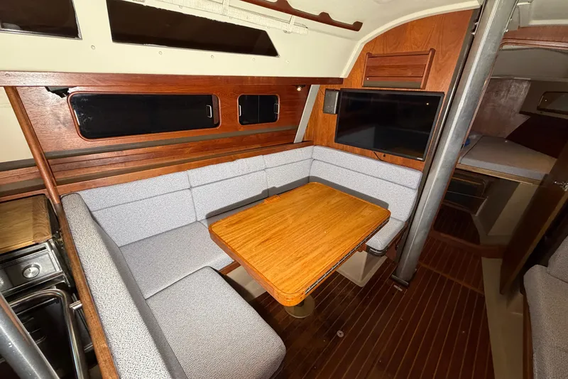 Slide: The Image of 1984 C&C 35-3 yacht interior with wood table, cushioned seating, and mounted TV. - 25