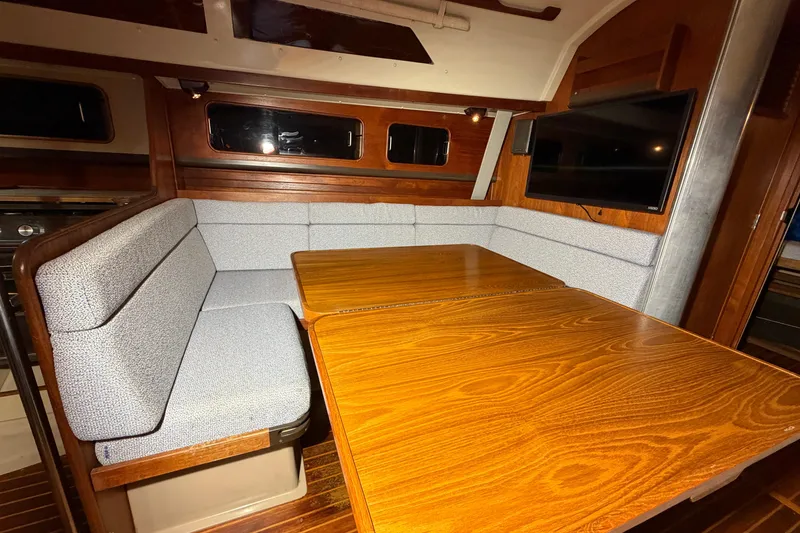 Slide: The Image of 1984 C&C 35-3 yacht interior with wooden table, cushioned seating, and mounted TV. - 26