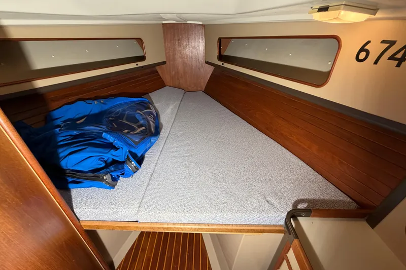 Slide: The Image of 1984 C&C 35-3 sailboat cabin interior with wooden paneling and blue jacket on bed. - 29
