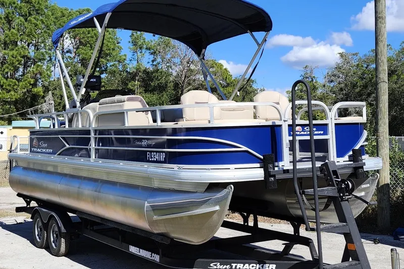 The Image of 2018 Sun Tracker Fishin' Barge 22 DLX pontoon boat on trailer, blue and silver design. - 1