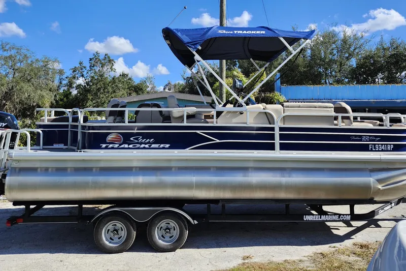 Slide: The Image of 2018 Sun Tracker Fishin' Barge 22 DLX pontoon boat on trailer, blue canopy, sunny day. - 11