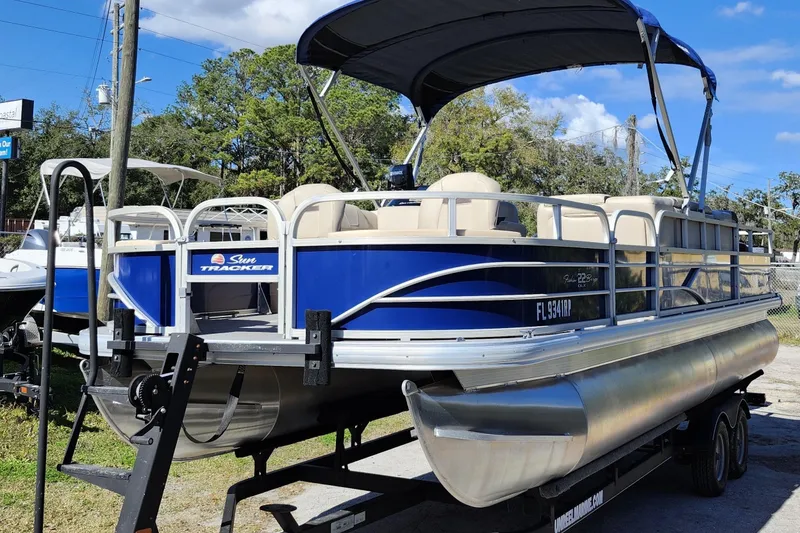 Slide: The Image of 2018 Sun Tracker Fishin' Barge 22 DLX pontoon boat on trailer, blue and silver design. - 3