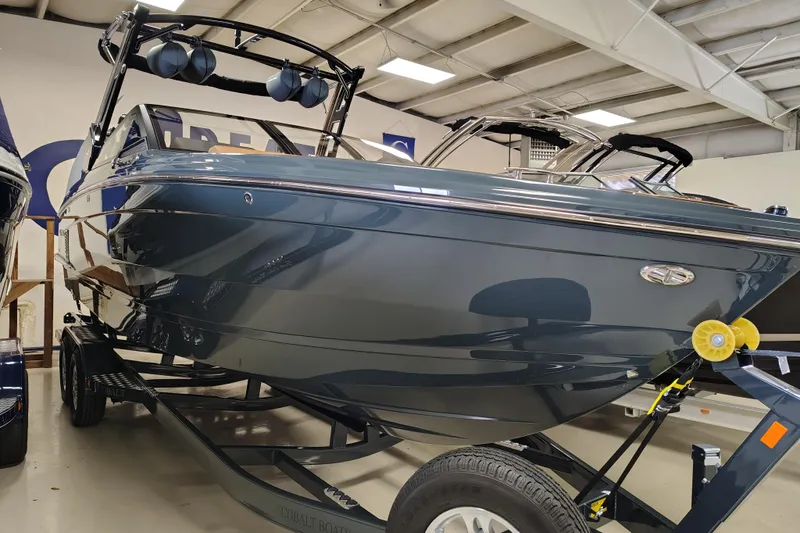 The Image of 2026 Cobalt R8 Surf boat in showroom, sleek design with trailer. - 1