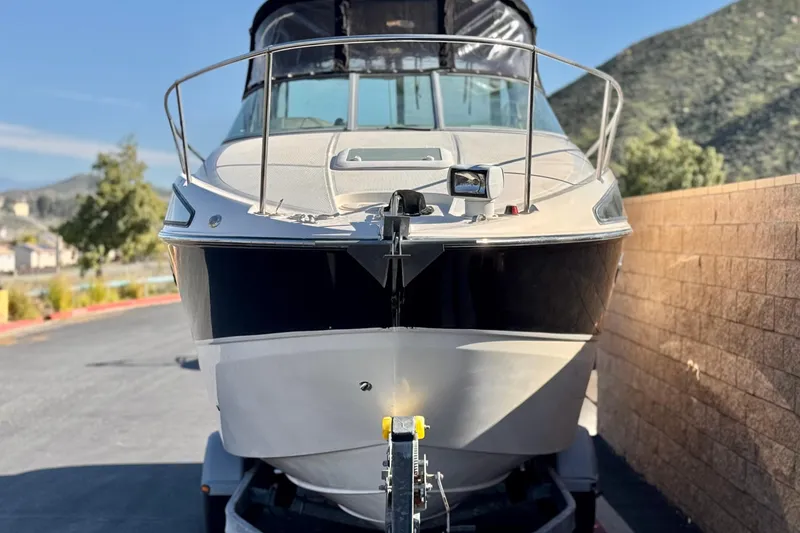 Slide: The Image of 2009 Bayliner 265 SB boat on trailer, parked near a brick wall, with scenic background. - 2