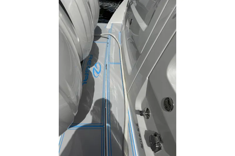 Slide: The Image of 2023 Regal 38 FXO boat deck with blue trim, docked on calm water. - 33
