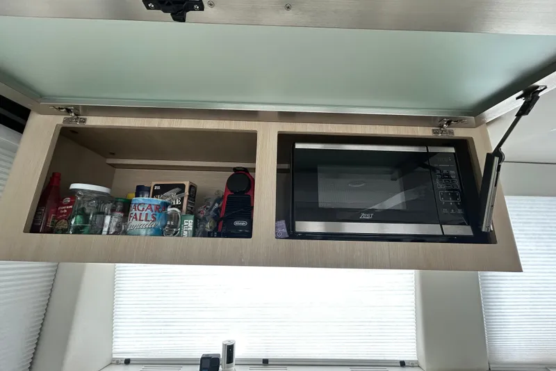 Slide: The Image of Open cabinet in 2023 Regal 38 FXO yacht with microwave and assorted items. - 88