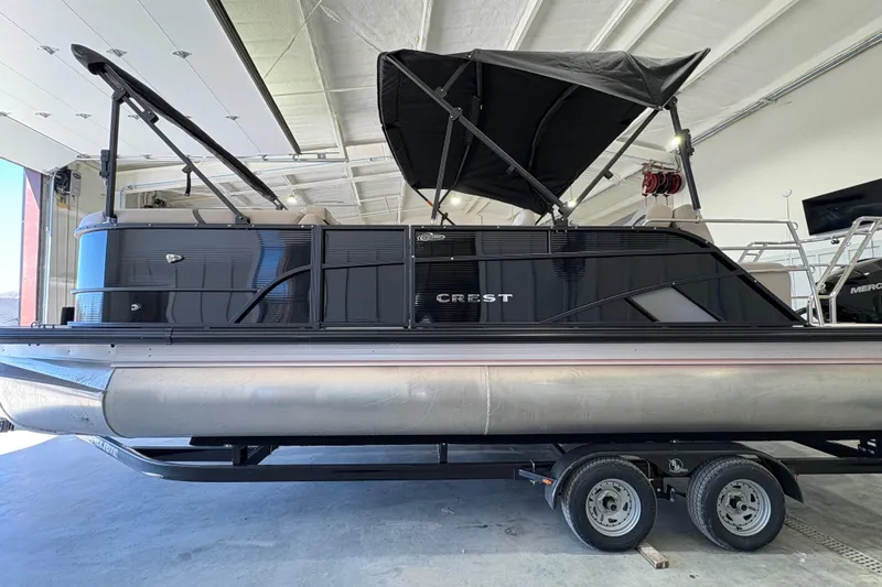 The Image of 2025 Crest Classic 220 pontoon boat with black exterior, parked indoors on a trailer. - 0