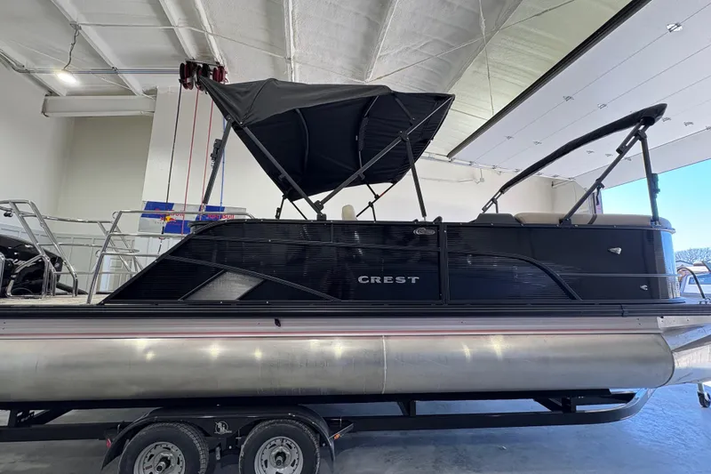 Slide: The Image of 2025 Crest Classic 220 pontoon boat with black canopy, displayed indoors on a trailer. - 2